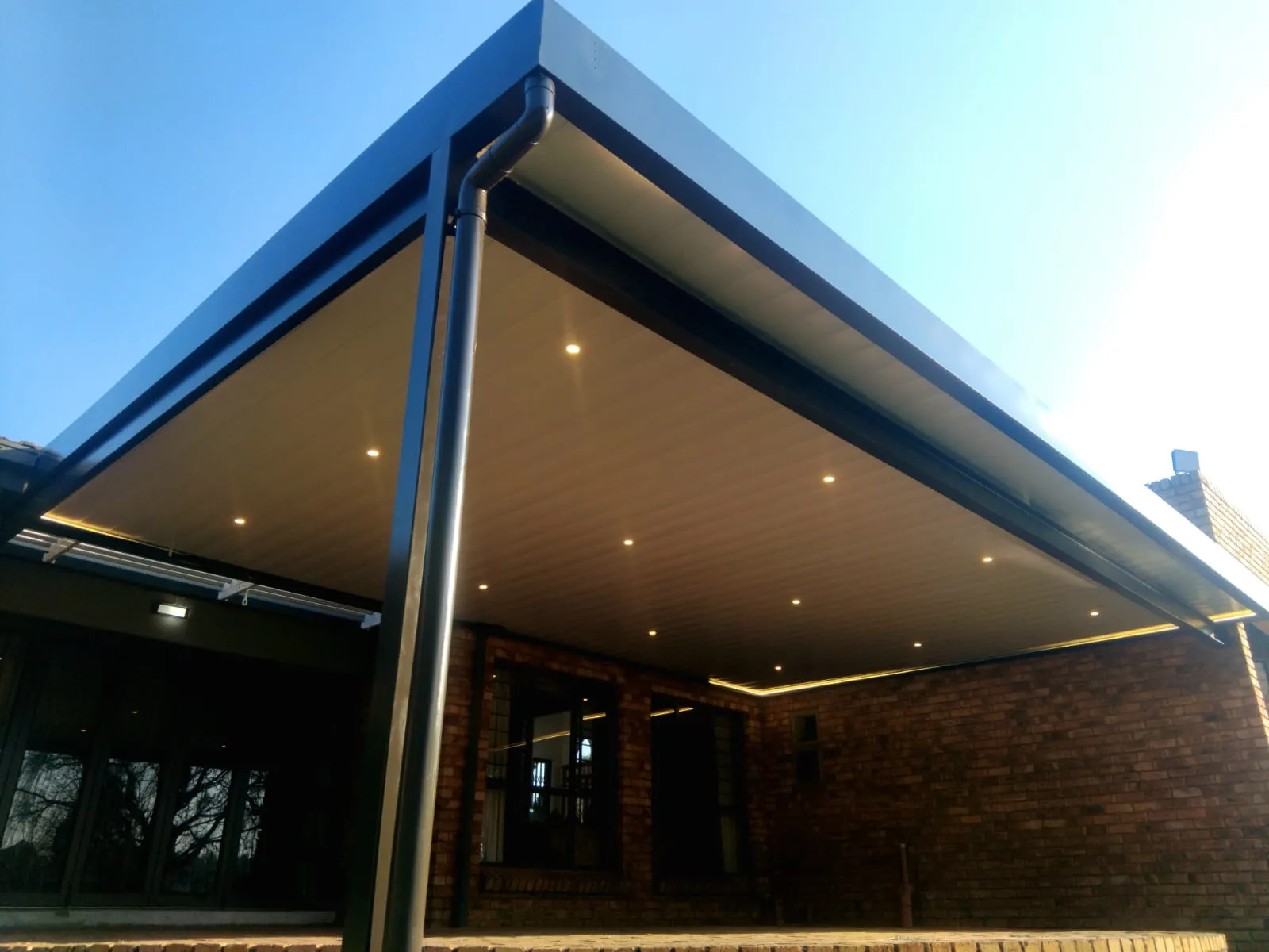 Ceiling awning patio cover with charcoal fascia and recessed downlights at a brick home