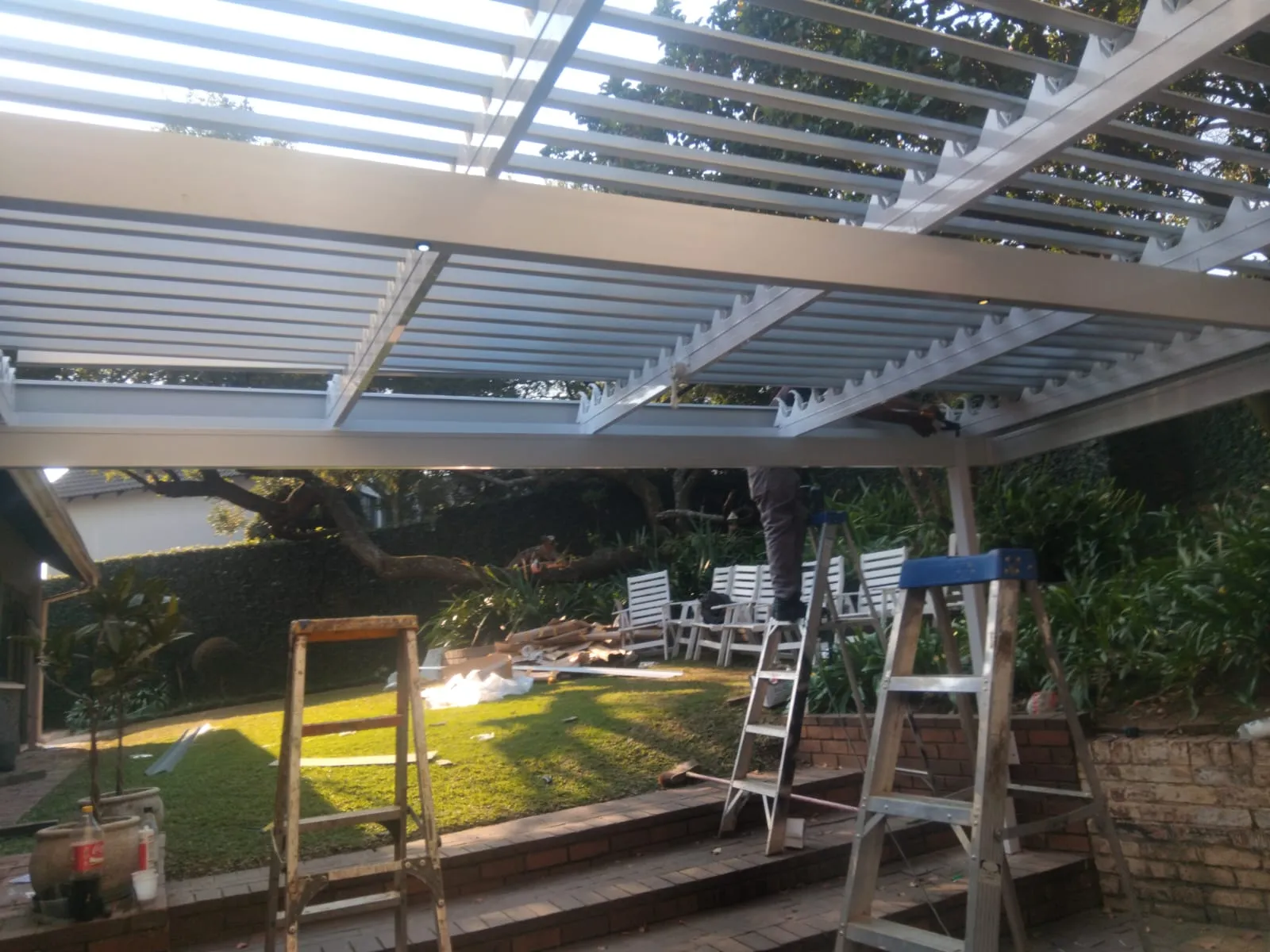 Installers fitting adjustable aluminium louvre blades to a patio awning