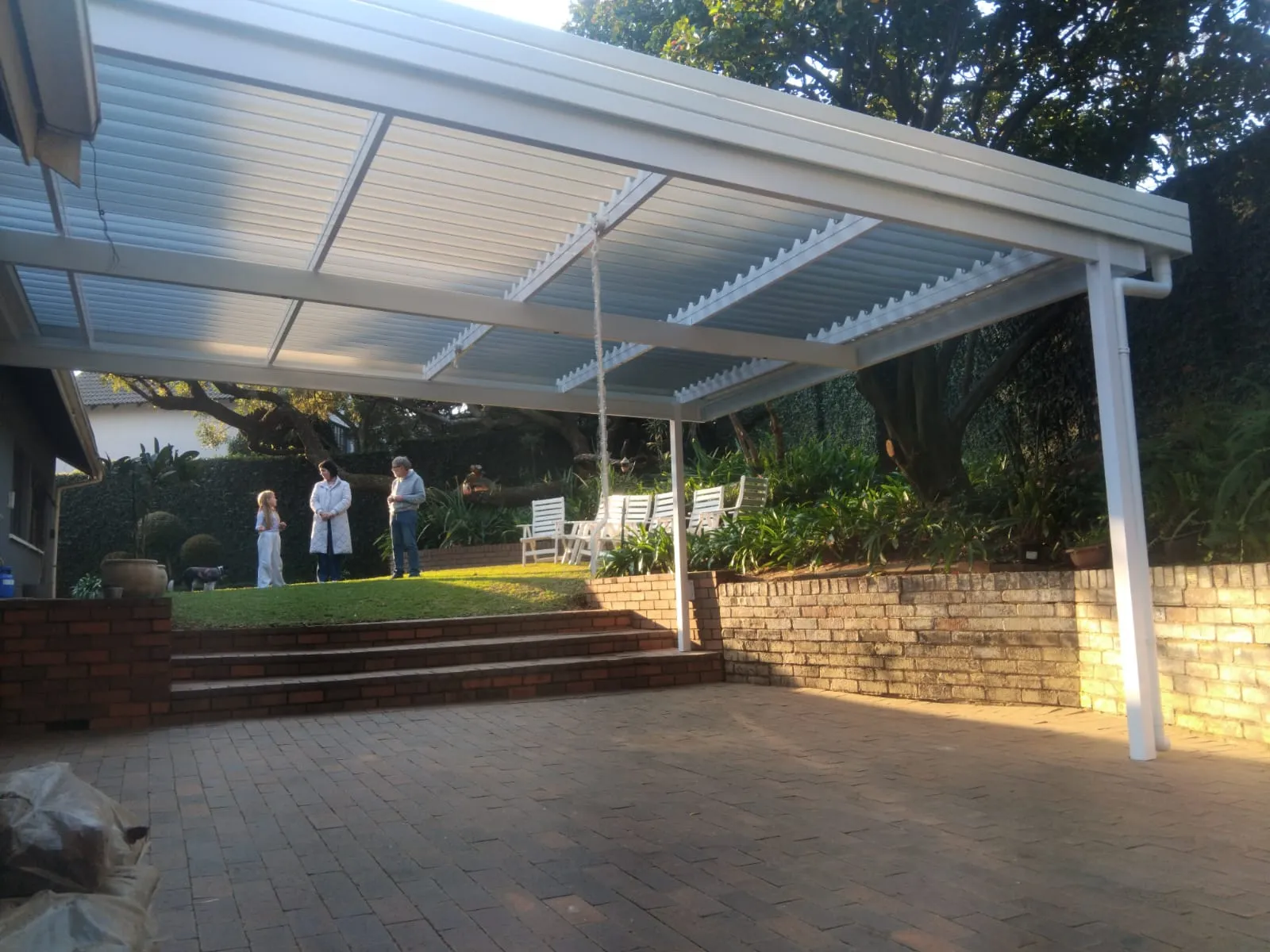 White louvre awning covering a large brick-paved patio with garden steps