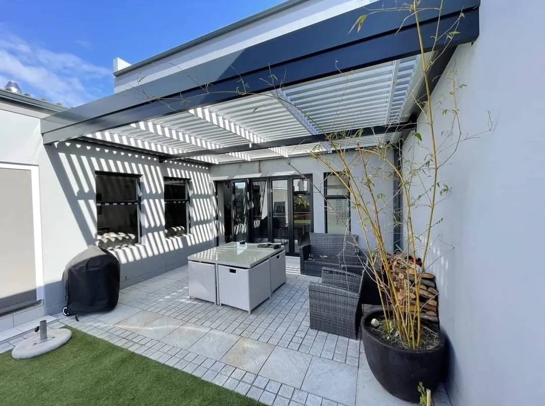 Open louvre blades casting striped shade over a courtyard patio and outdoor kitchen